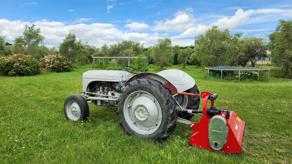A restored grey Ferguson tractor with a red flail mulcher attached to its three-point linkage