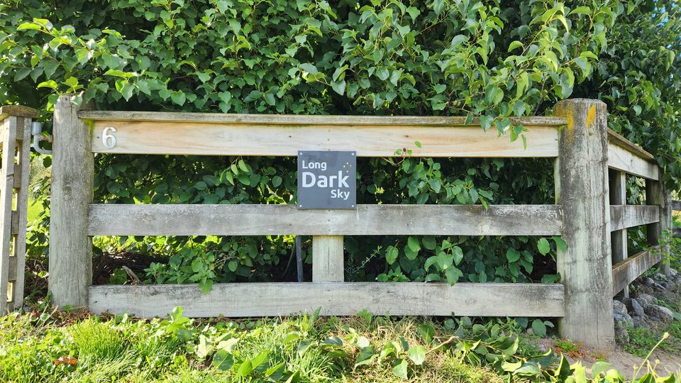 A slate Long Dark Sky sign mounted on a timber post-and-rail gate surrounded by greenery