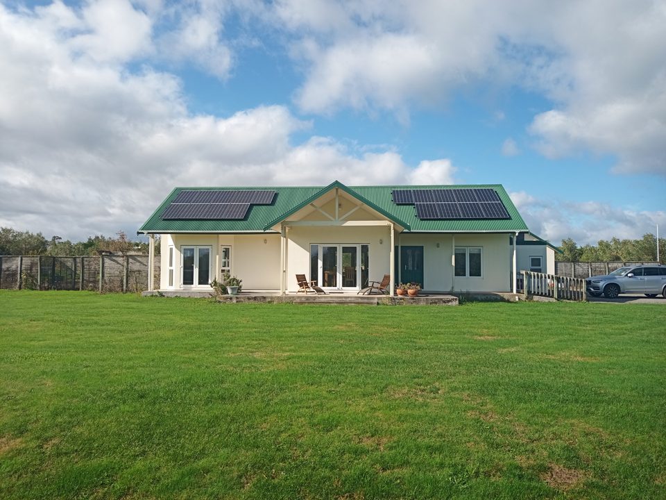 The front of the house across a wide green lawn, with solar panels on a green roof