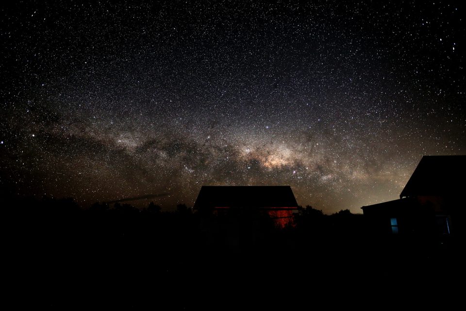 A broad band of the Milky Way low over silhouetted farm sheds