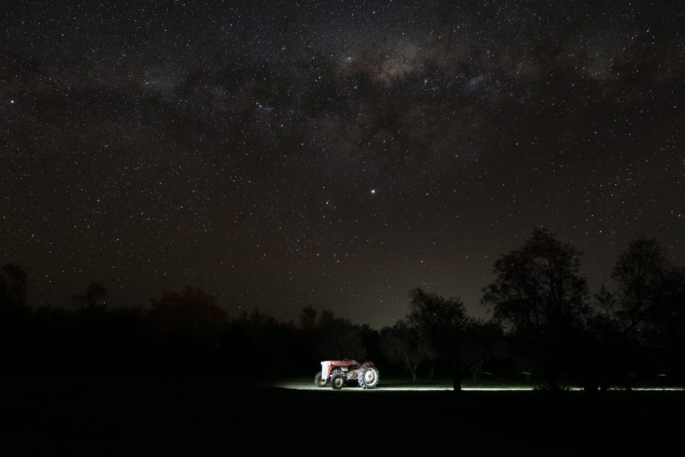 A vintage tractor lit by torchlight beneath the Milky Way