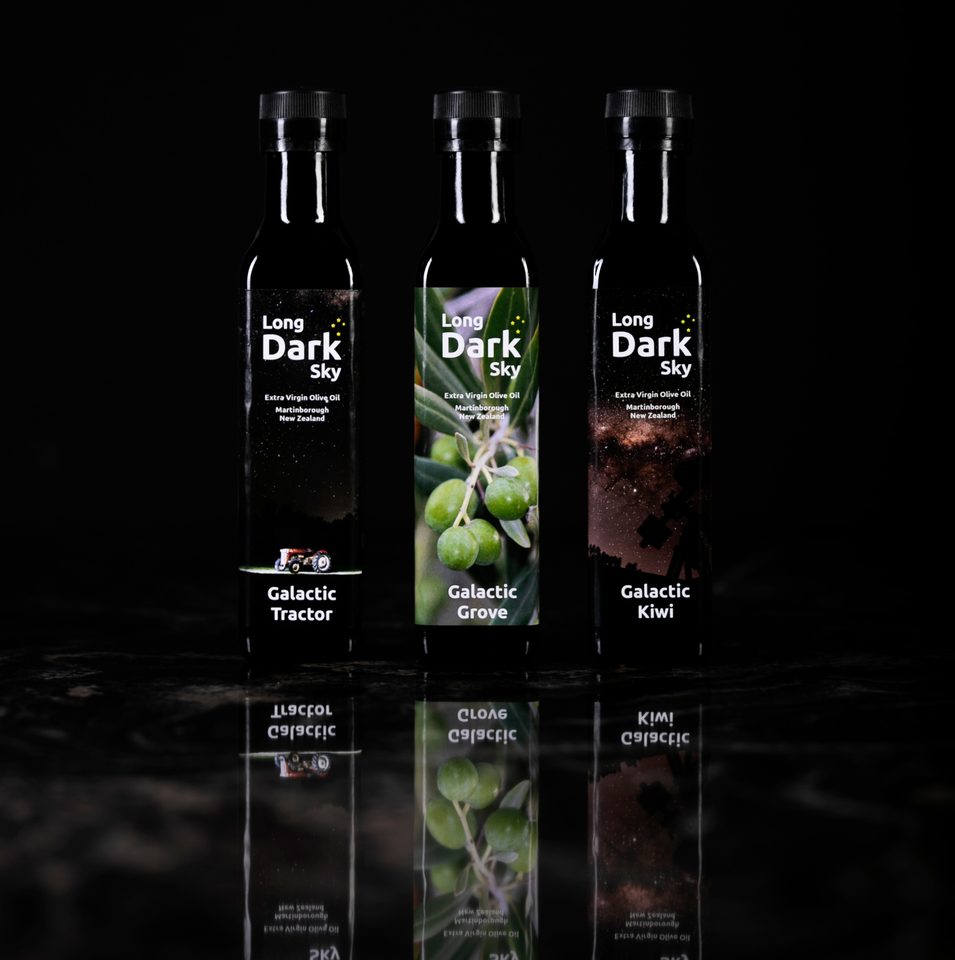 Three bottles of Long Dark Sky extra virgin olive oil on a black reflective surface