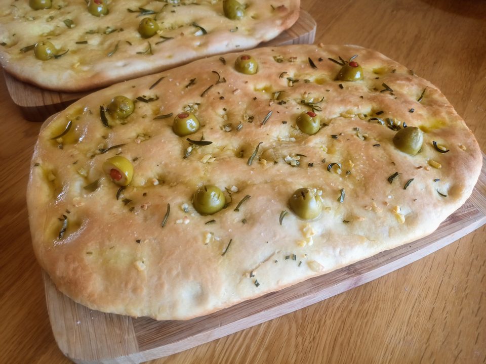 Two golden focaccia loaves studded with green olives and rosemary